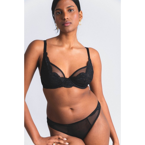 A clean, studio-lit photograph featuring a model wearing a black lace bra and matching panty set against a neutral white background.